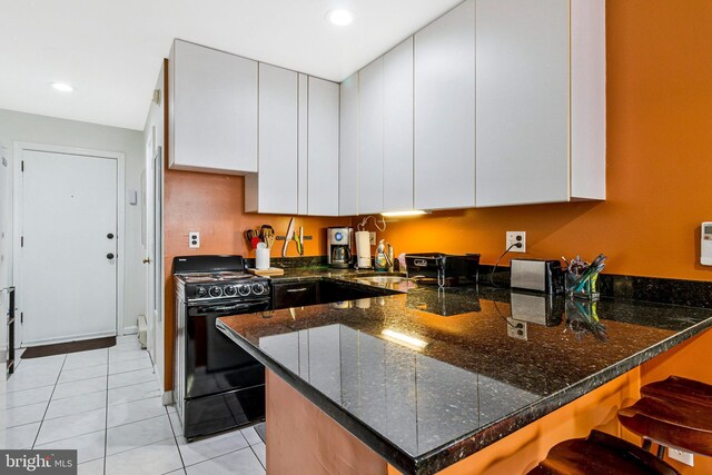 kitchen with dark stone counters, light tile patterned floors, a peninsula, black range with gas cooktop, and white cabinetry