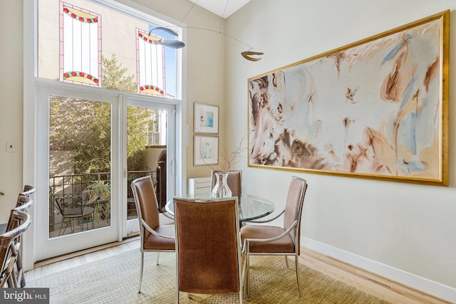 dining space featuring baseboards, wood finished floors, and a towering ceiling