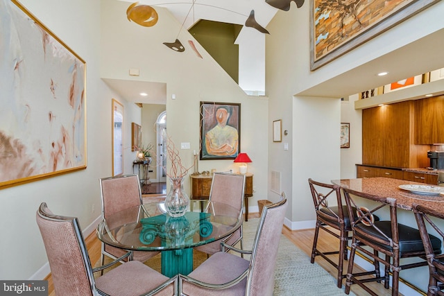 dining room with visible vents, a high ceiling, baseboards, and light wood-type flooring