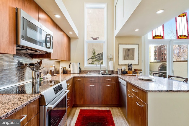 kitchen with light stone counters, a peninsula, a sink, light wood-style floors, and appliances with stainless steel finishes