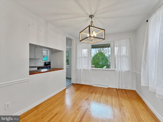 unfurnished dining area featuring baseboards, a notable chandelier, baseboard heating, and light wood finished floors