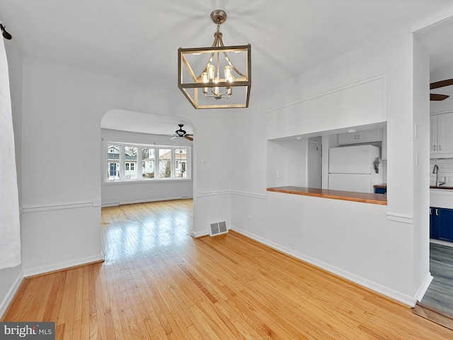 unfurnished dining area featuring visible vents, baseboards, ceiling fan with notable chandelier, hardwood / wood-style flooring, and a sink