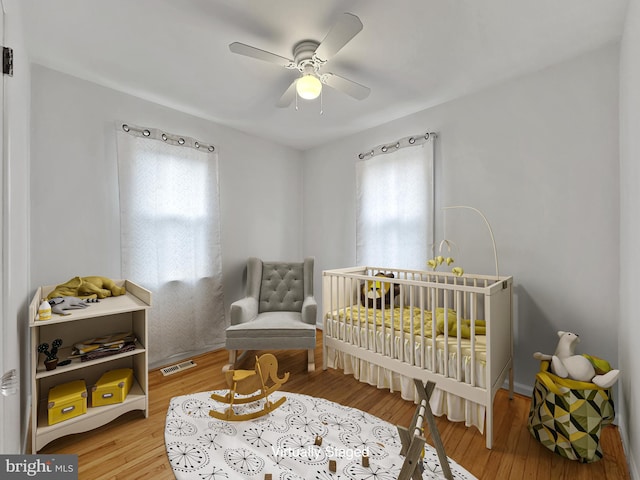 bedroom with light wood finished floors, visible vents, a ceiling fan, and a nursery area