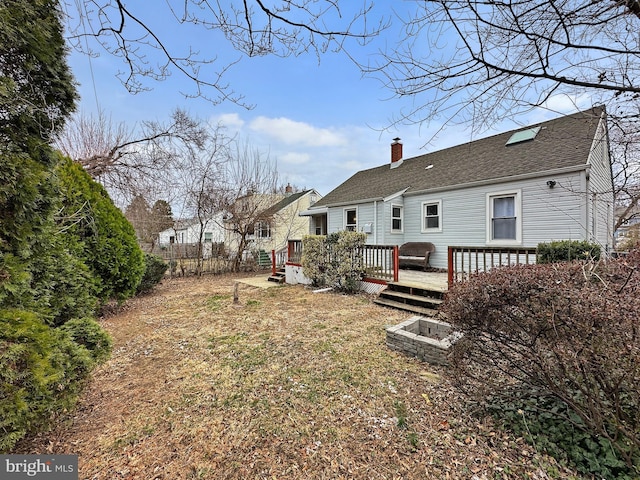 back of house with a chimney, a deck, and a shingled roof