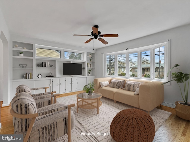 living area featuring built in features, light wood-type flooring, baseboards, and ceiling fan