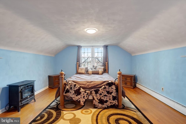 bedroom featuring baseboards, baseboard heating, light wood-style flooring, and a wood stove