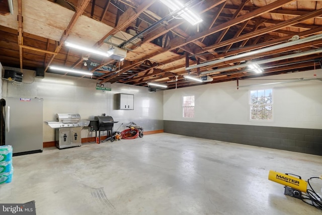 garage with concrete block wall, a garage door opener, and freestanding refrigerator