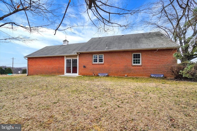 back of house featuring brick siding, a lawn, and roof with shingles