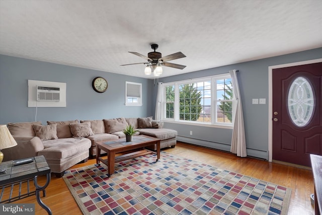 living area featuring wood finished floors, ceiling fan, a wall mounted air conditioner, a textured ceiling, and a baseboard heating unit