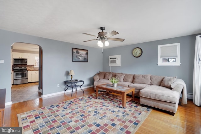 living area featuring baseboards, a ceiling fan, arched walkways, and light wood-type flooring