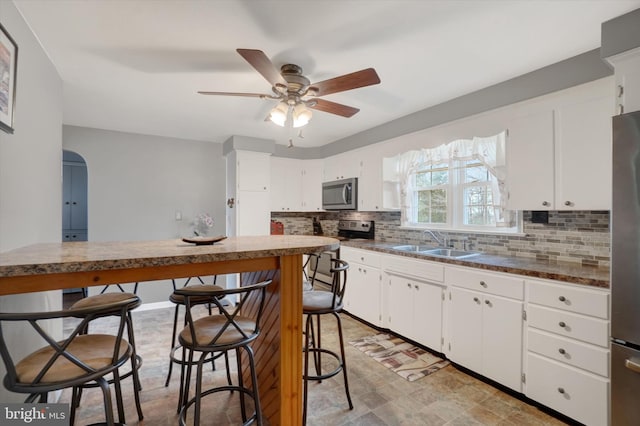 kitchen with a sink, stainless steel appliances, decorative backsplash, and white cabinetry