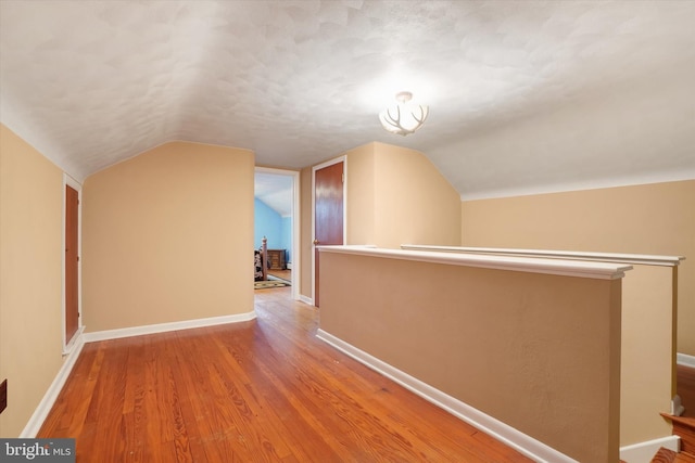 hall with vaulted ceiling, wood finished floors, and baseboards