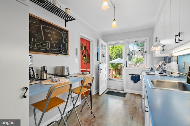 kitchen featuring white cabinets, a sink, wood finished floors, under cabinet range hood, and ornamental molding