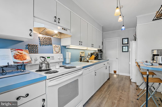 kitchen featuring crown molding, a sink, light countertops, under cabinet range hood, and white appliances