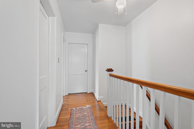 hall featuring light wood-style floors, baseboards, and an upstairs landing