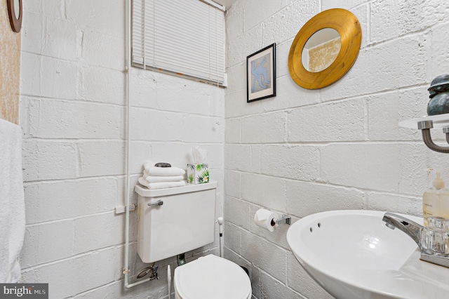 half bath with a sink, toilet, and concrete block wall