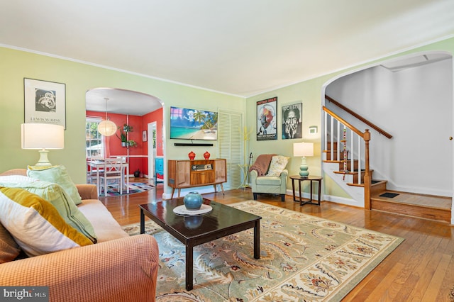 living area featuring crown molding, arched walkways, stairs, and hardwood / wood-style flooring