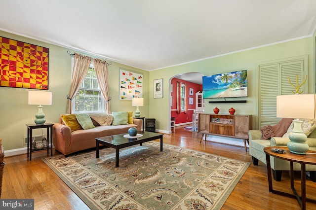 living room featuring crown molding, arched walkways, baseboards, and hardwood / wood-style floors