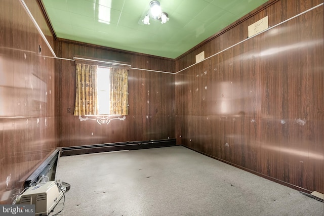 spare room featuring a baseboard heating unit, wood walls, and carpet flooring