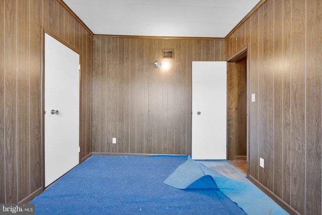 unfurnished room with carpet flooring, visible vents, and wood walls