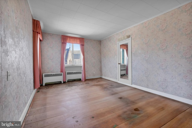 unfurnished room with baseboards, hardwood / wood-style flooring, radiator heating unit, and wallpapered walls