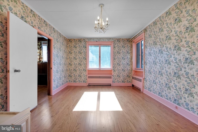 empty room featuring wallpapered walls, radiator, light wood-style floors, and ornamental molding