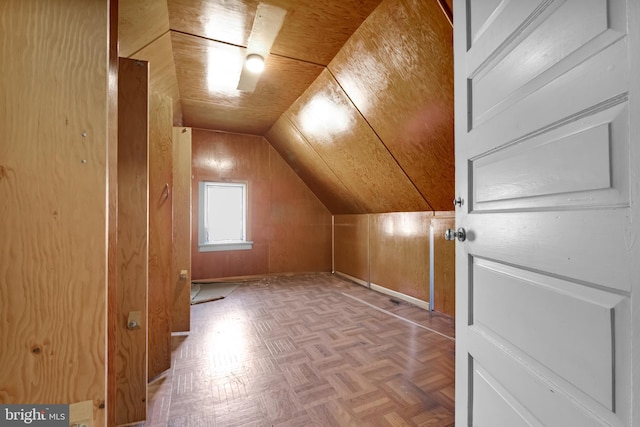 additional living space with vaulted ceiling, baseboards, and wood walls