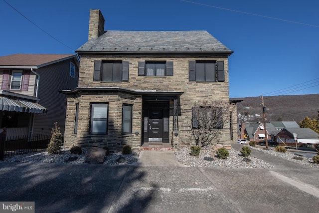 view of front facade with a high end roof, a chimney, and stone siding