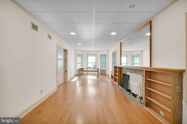 unfurnished living room featuring visible vents, baseboards, a fireplace with flush hearth, a drop ceiling, and light wood-style floors