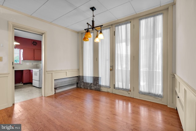 unfurnished dining area featuring a wainscoted wall, light wood finished floors, ornamental molding, an inviting chandelier, and a decorative wall