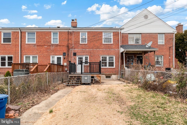 back of property with a deck, brick siding, a fenced backyard, and a chimney