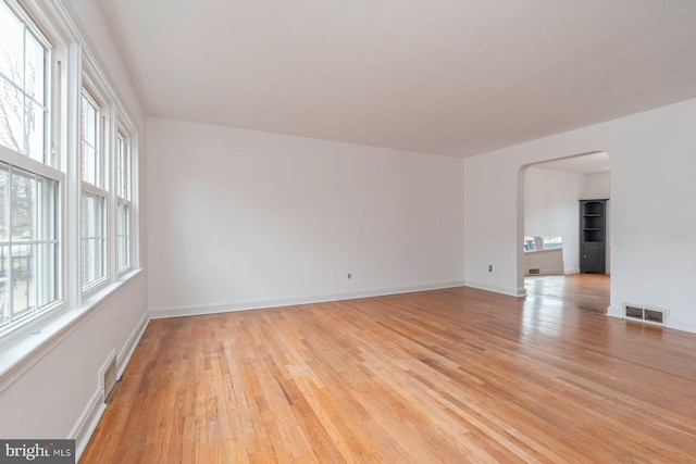 unfurnished room with light wood-style floors, arched walkways, visible vents, and baseboards