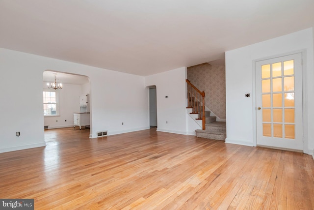 unfurnished living room with arched walkways, visible vents, light wood-style flooring, and an inviting chandelier