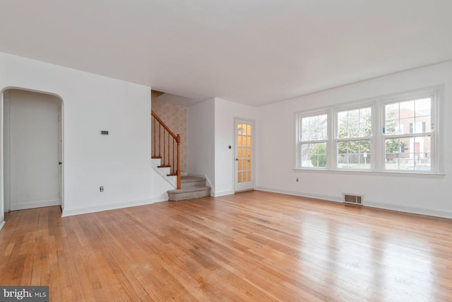 unfurnished living room featuring stairway, baseboards, visible vents, arched walkways, and light wood-type flooring