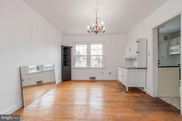 unfurnished dining area featuring a notable chandelier, visible vents, and light wood-style flooring