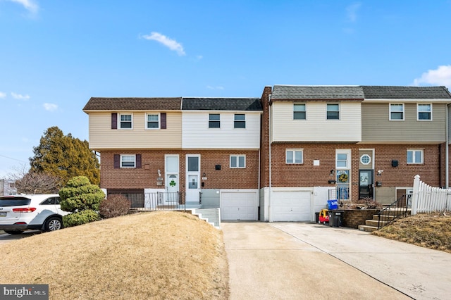 multi unit property featuring brick siding, concrete driveway, an attached garage, and a shingled roof