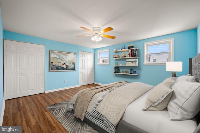 bedroom with ceiling fan, wood finished floors, multiple closets, and baseboards