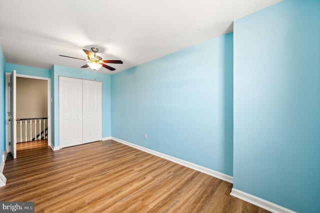 unfurnished bedroom with a closet, a ceiling fan, baseboards, and wood finished floors