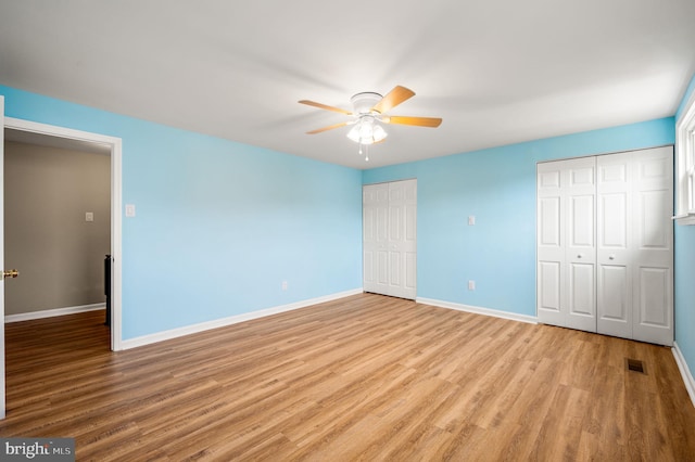 unfurnished bedroom featuring visible vents, baseboards, ceiling fan, light wood-style floors, and multiple closets