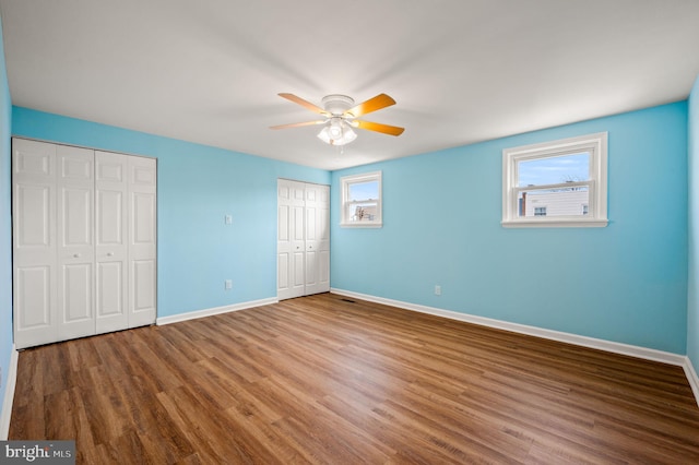 unfurnished bedroom with ceiling fan, two closets, baseboards, and wood finished floors