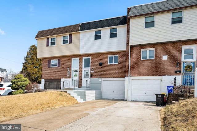 multi unit property with driveway, mansard roof, an attached garage, a shingled roof, and brick siding