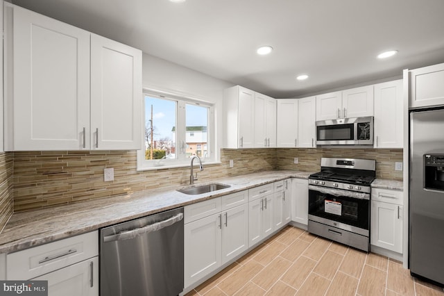 kitchen featuring tasteful backsplash, white cabinetry, stainless steel appliances, and a sink