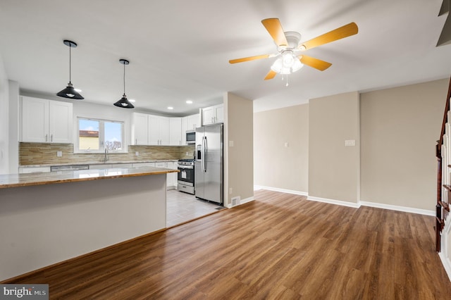 kitchen with backsplash, stainless steel appliances, light wood-style floors, white cabinets, and light stone countertops