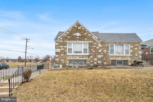 back of property featuring fence, a lawn, stone siding, and a shingled roof