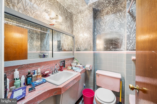 bathroom featuring toilet, tile walls, wainscoting, wallpapered walls, and vanity