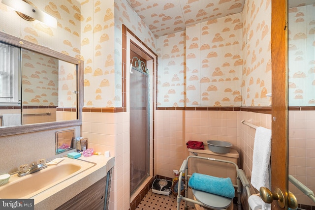 full bathroom featuring vanity, a wainscoted wall, wallpapered walls, a shower stall, and tile walls