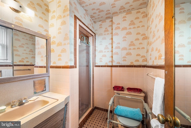 bathroom with vanity, a wainscoted wall, wallpapered walls, a stall shower, and tile walls