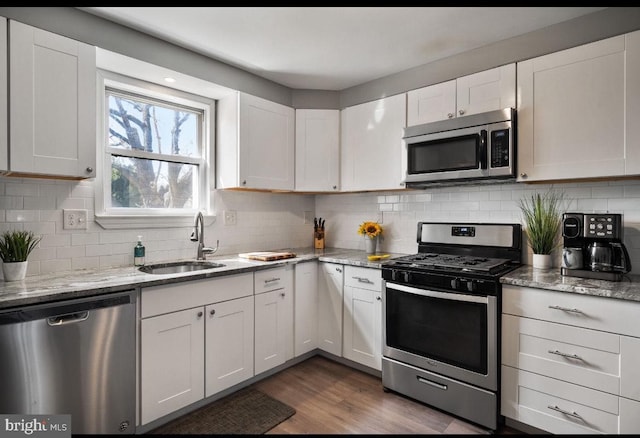 kitchen with light stone counters, a sink, white cabinets, appliances with stainless steel finishes, and backsplash