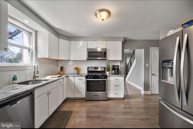 kitchen with a sink, stainless steel appliances, light stone counters, and white cabinets