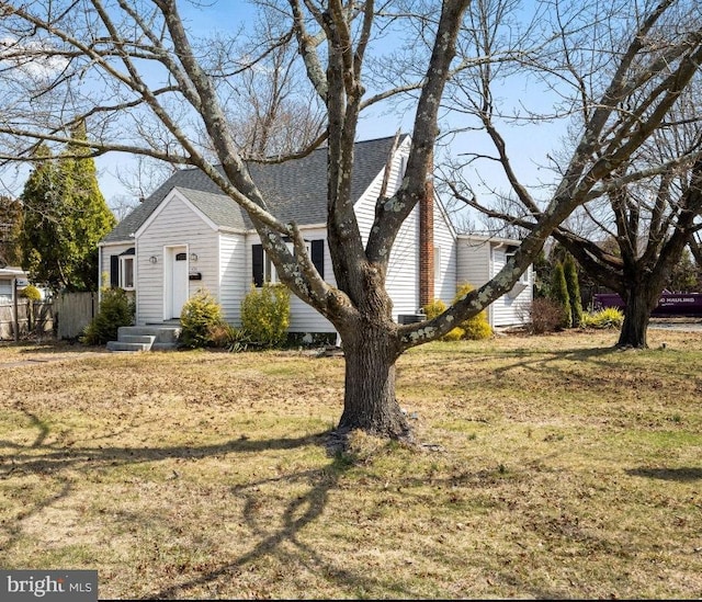 view of front of house with roof with shingles, a front yard, and fence